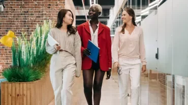 Three colleagues walking and talking in a modern office corridor.