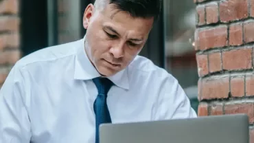 Man in white shirt and tie working on a laptop outdoors.