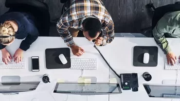 Top view of three people working at white desks with computers and headsets in an office.