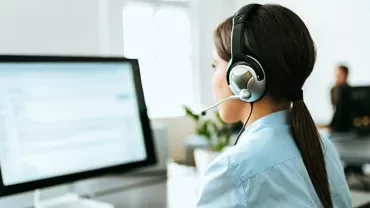 Woman wearing headset working at a computer in an office.