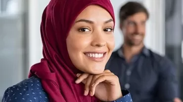 Smiling woman in a red hijab with colleagues in the background.