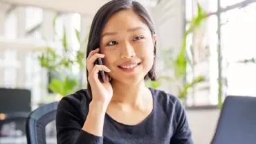 female Chinese white-collar professional in her 30s answering her mobile phone while sitting in front of the laptop