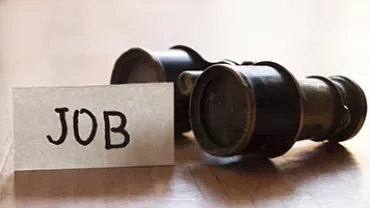 Close-up of binoculars next to a card reading 'JOB'.