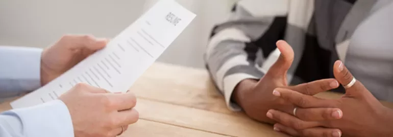 Close-up of a job interview with resume and gesturing hands at a table.